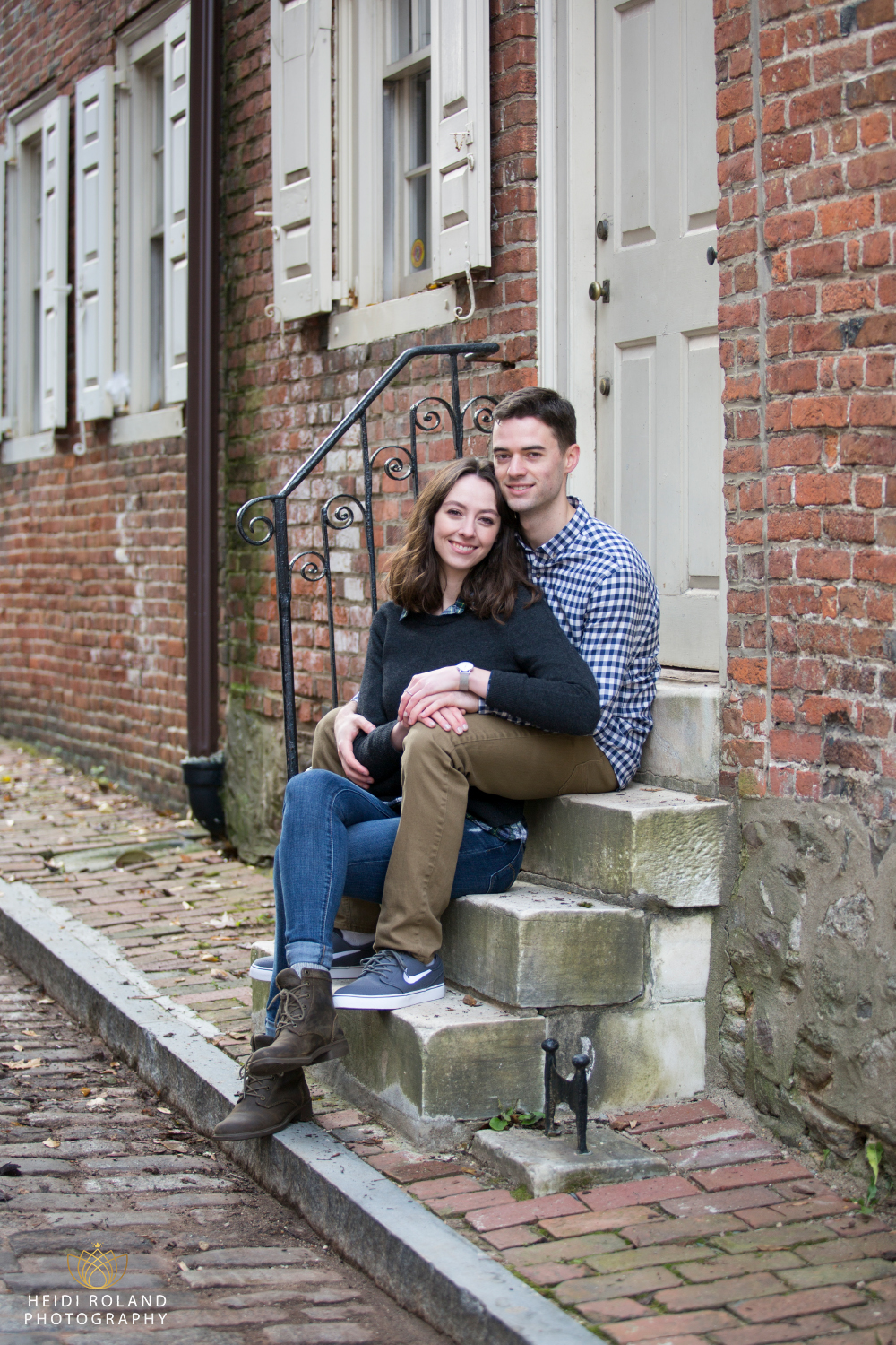 Couple sit on cobblestone street engagement session Philadelphia