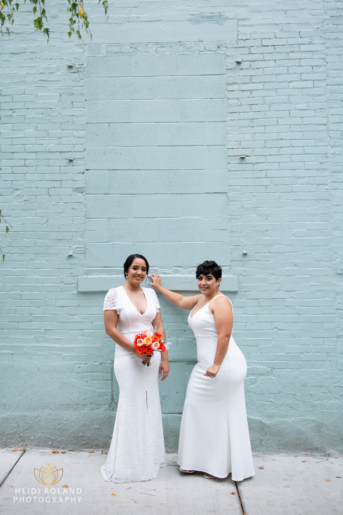 wedding portraits of two brides in front of blue painted building in Philadelphia