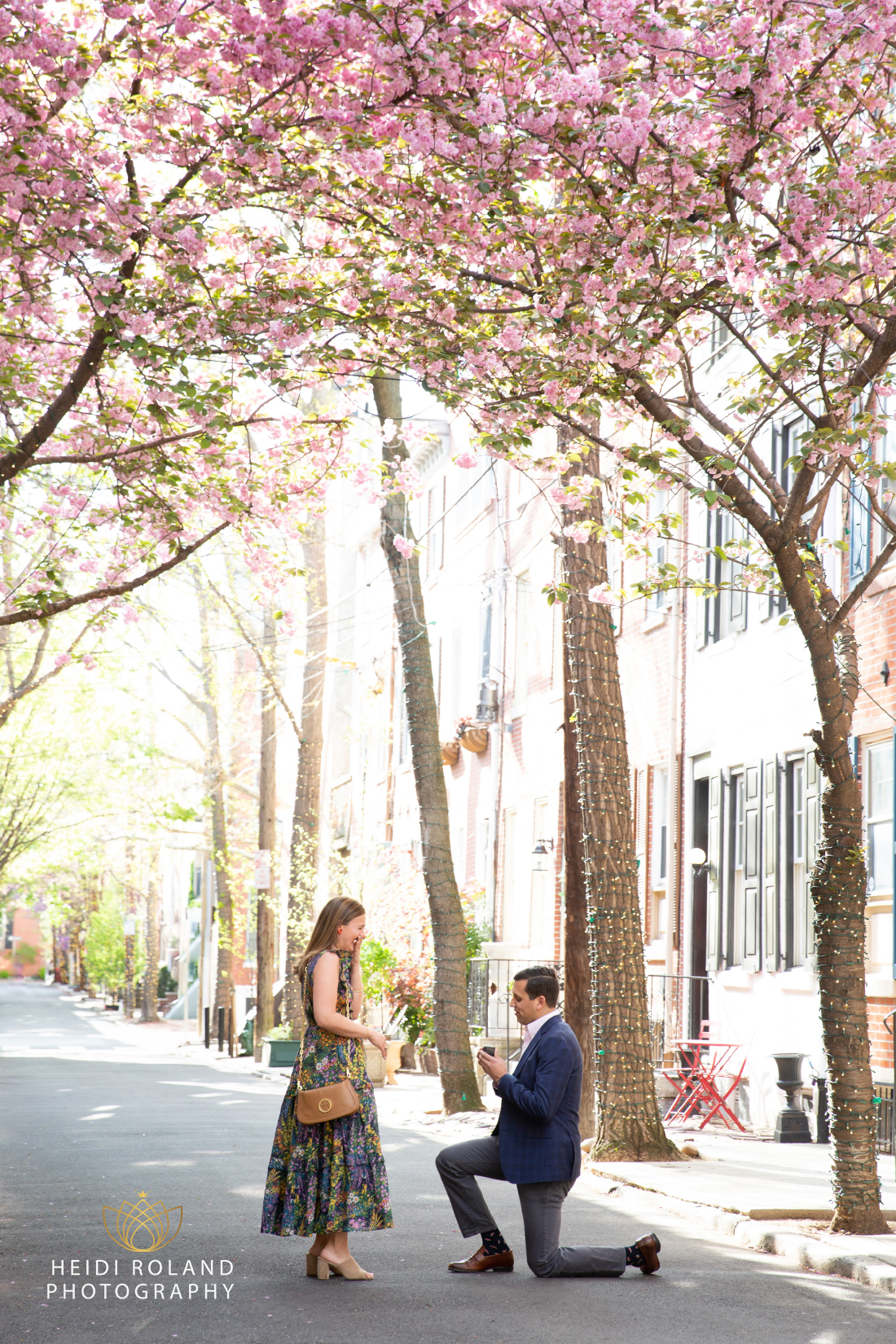 Man on one knee proposing to woman surrounded by cherry blossoms in Philly