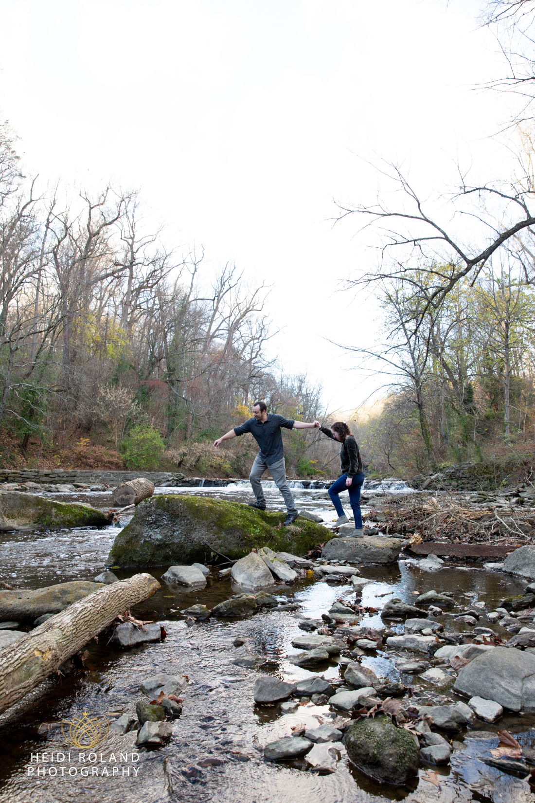 Couple walking across rocks in a river at Wissahickon Valley Park in Philadelphia